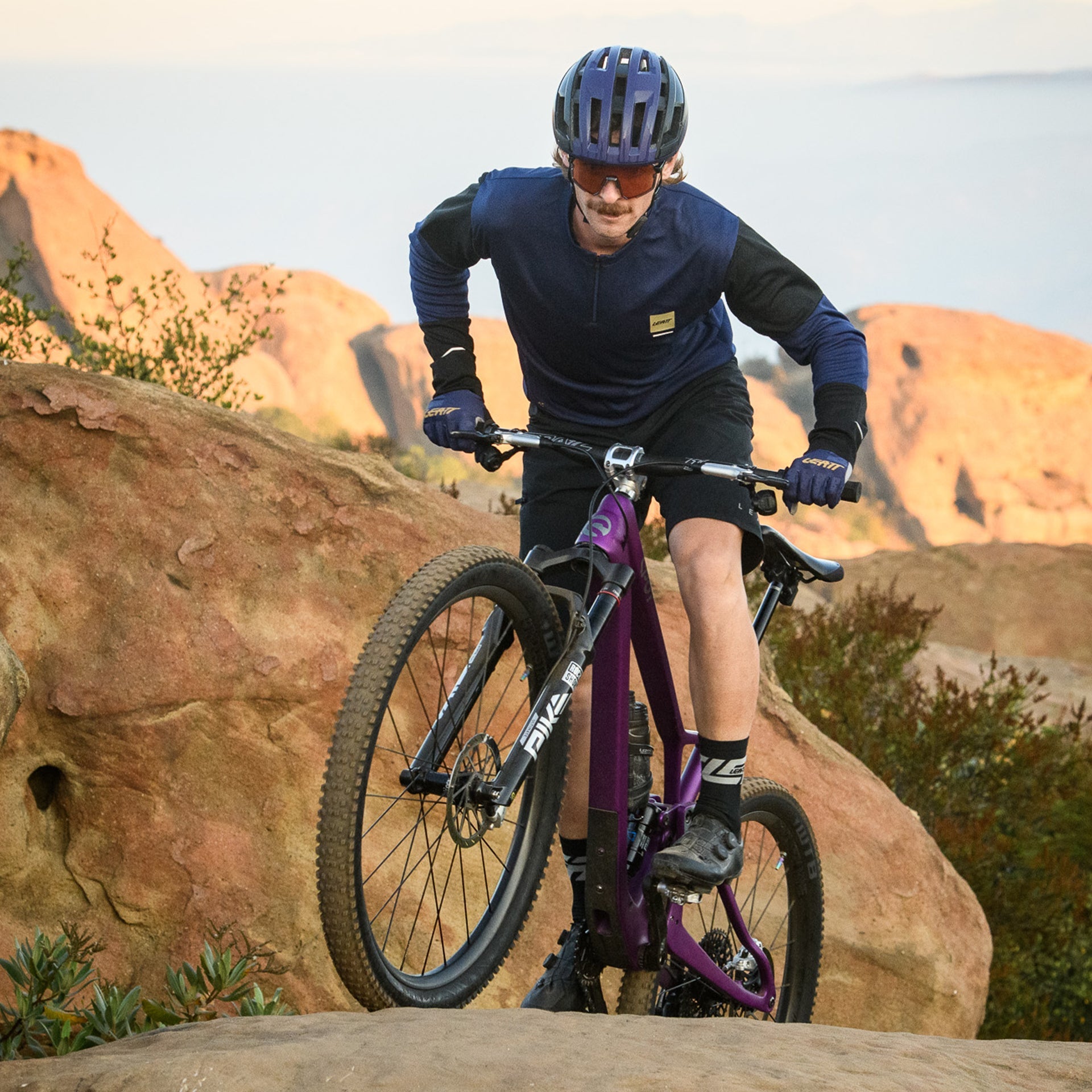 Person riding a mountain bike on rocky terrain with desert landscape in the background